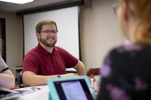 An education student smiles while working with peers as they sit at a classroom table. 