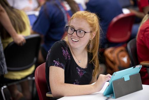 A student smiles while sitting and working on a tablet during an education class.  
