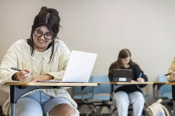 an education major sits in class, smiling and taking notes