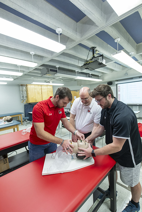 Two students and a professor work on a respiratory dunny.