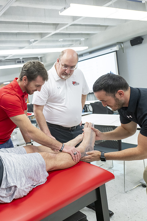 Two students show how to measure the angle of a foot to a teacher.