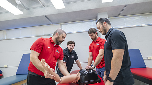 Three students watch a teacher show how to position an arm.