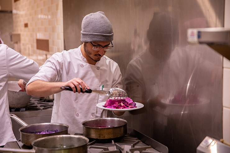 A food science student is holding a plate of something purple above a stove.