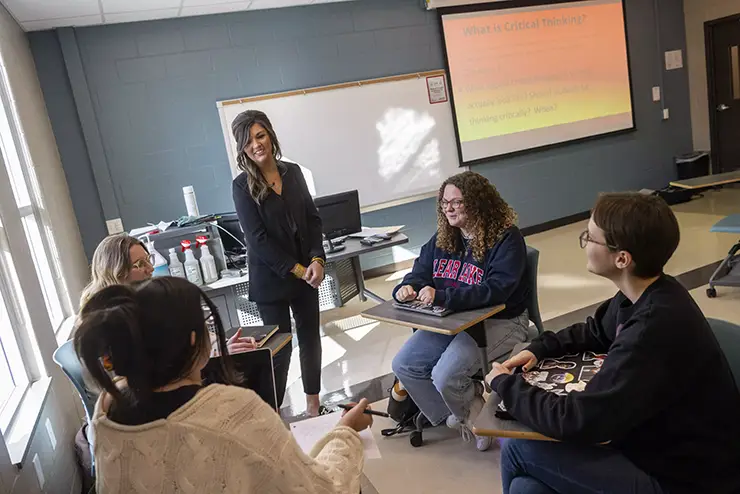 a university professor stands with a group of education students having a discussion