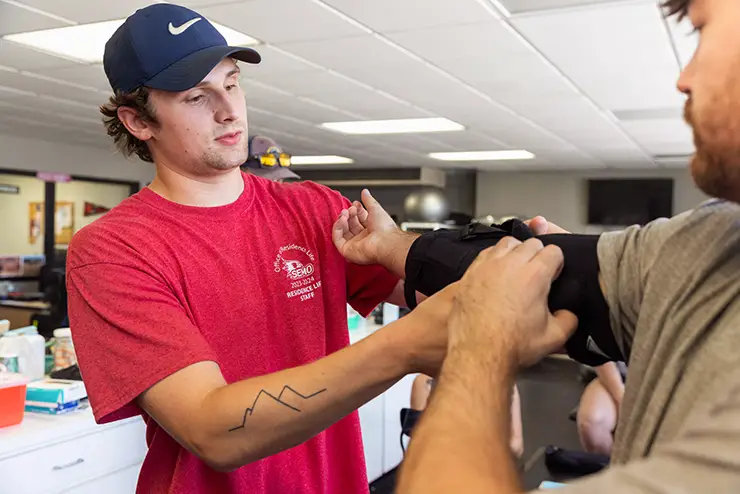 an athletic training degree student practices putting a brace on a classmate's arm