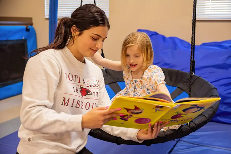 a communication disorders major reads a book to a child in a clinic setting