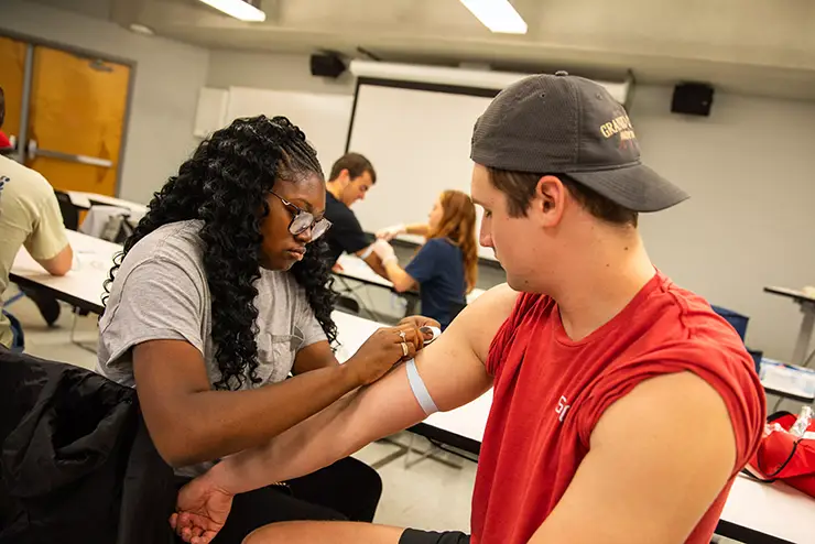 an athletic training major ties a tourniquet on a classmate's arm 