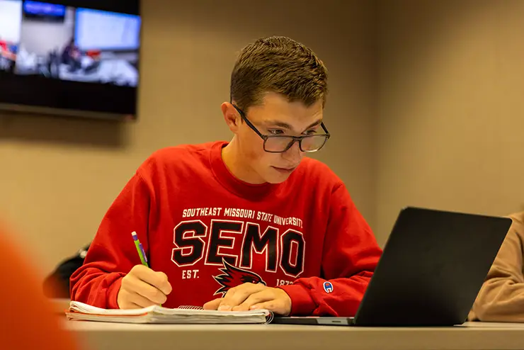 a SEMO student studies with his laptop and notebook in front of him 