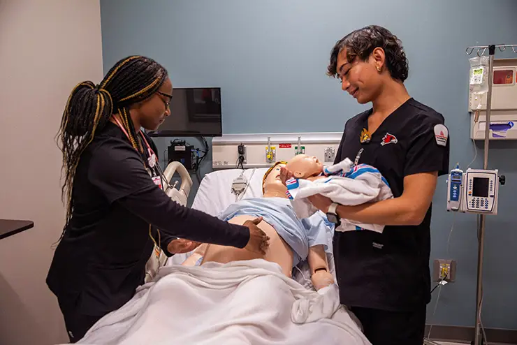 two SEMO nursing degree students work together over a manikin simulating birth
