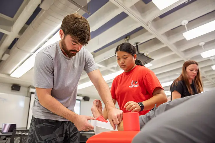 an athletic training student tapes the foot of a classmate