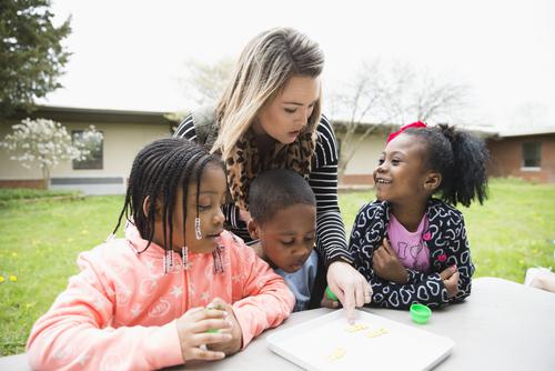A student teacher at Jefferson Elementary interacts with three students outside at a picnic table.