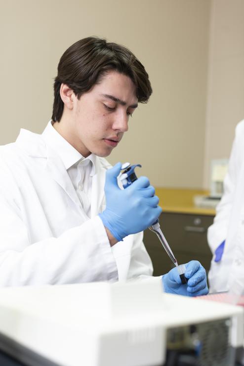 A Psychology student in a lab coat uses a syringe to fill up a small vial.