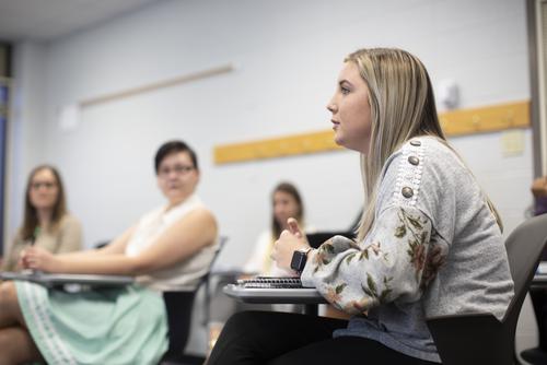 A missouri Psychology student sitting in a desk engages in a discussion with classmates.