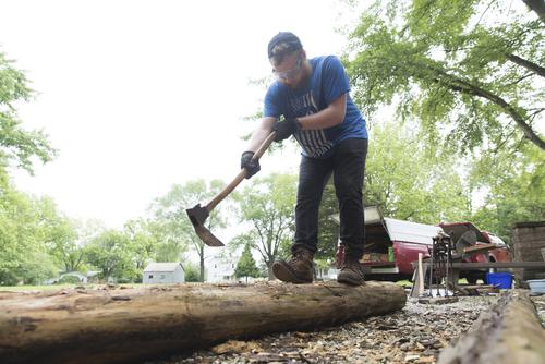 A Historic Preservation student works on refining a log for timber framing.