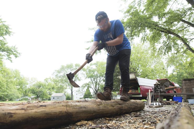 A Historic Preservation student works on refining a log for timber framing.