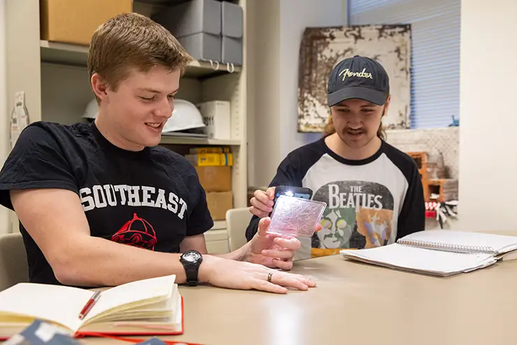 two students work together on a project - one holds up an item and the other shines his phone light on it at semo a Missouri college known for job readiness