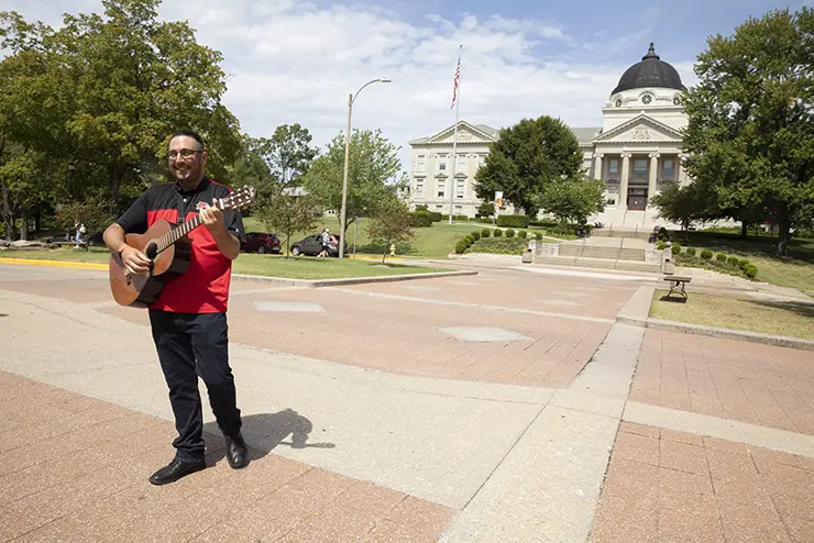 a hispanic individual stands in front of academic hall playing a guitar at semo a Missouri college known for job readiness