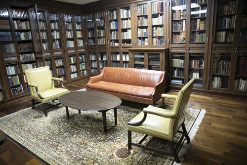 A couch and two chairs sit in the middle of a room surrounded by bookshelves.