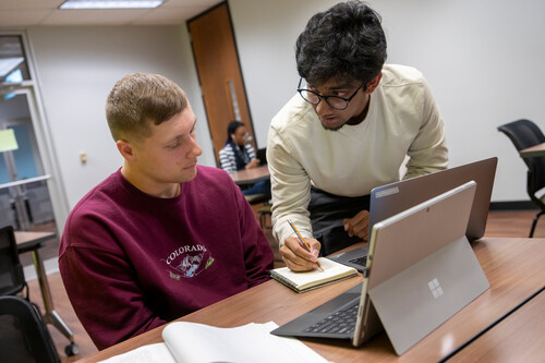Two students study together with their computers.