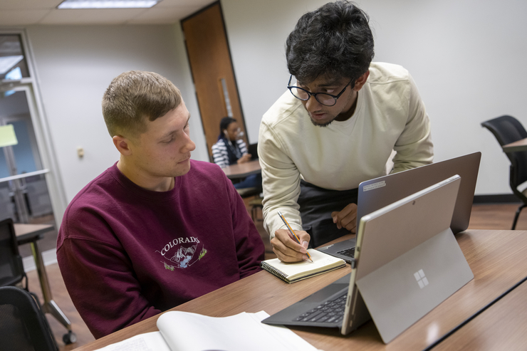 Two students study together with their computers.
