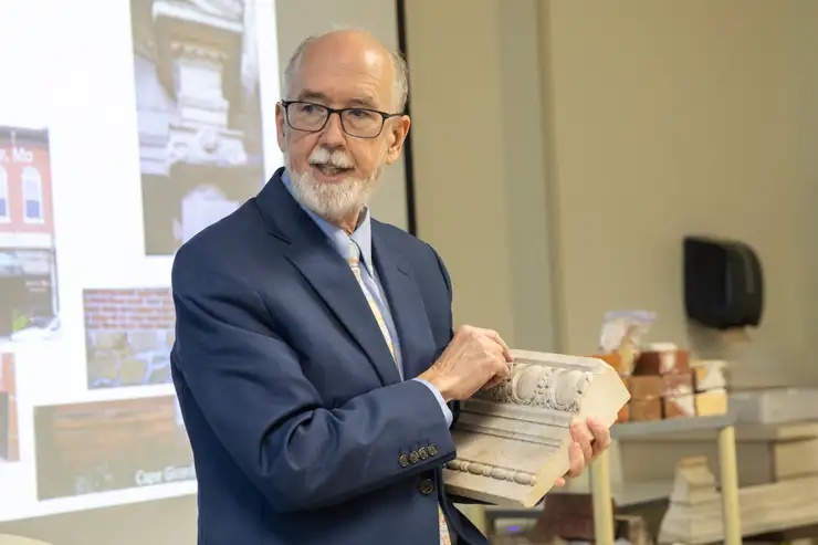 A Historic Preservation graduate professor holds a historic piece of a building and lectures to the class. 