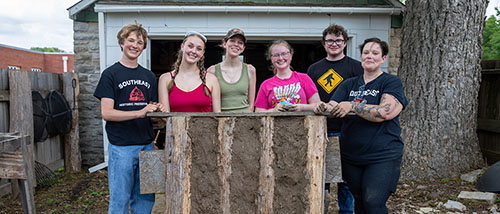 The historic preservation group poses beside the wood and mud wall they built together on the field trip.