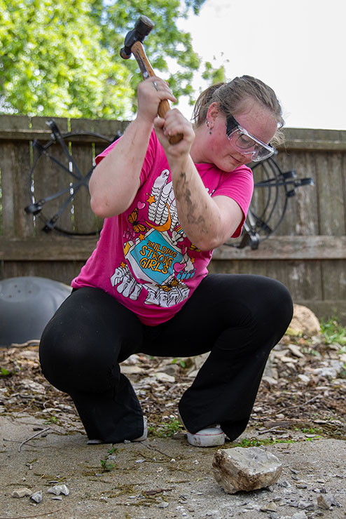 Participant of the historical preservation field trip uses a hammer to hit rocks.