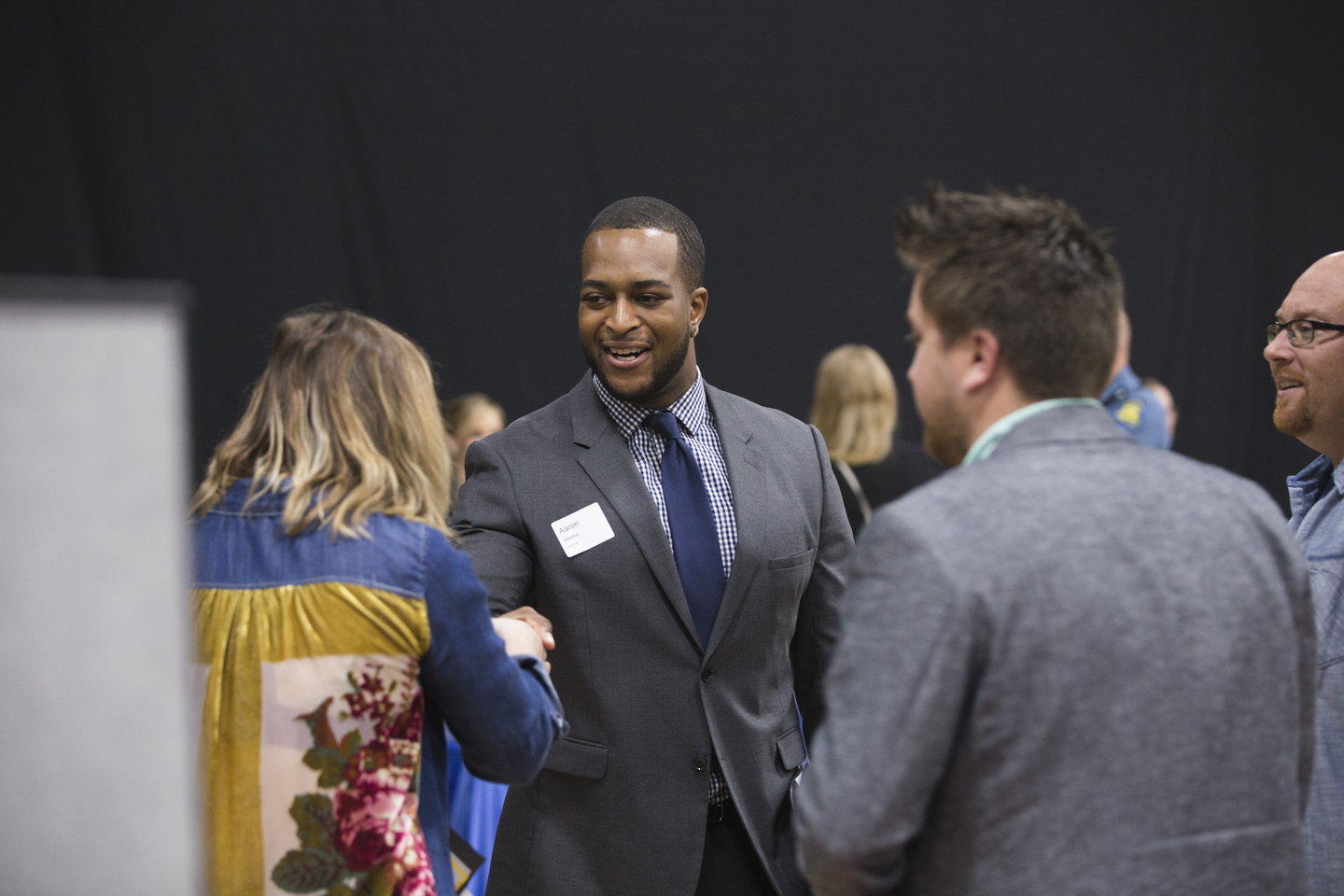 A student shakes hands with an individual while mingling at a career expo.