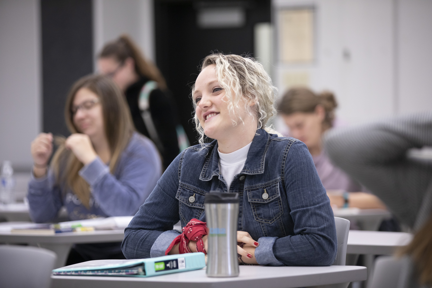 A student smiles while sitting at a desk and listening during class.