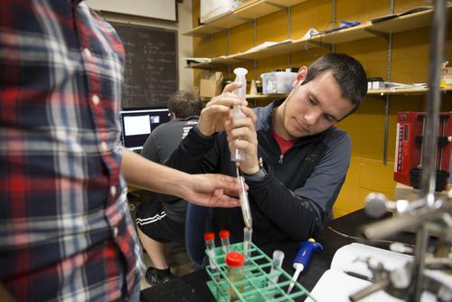 A student handles vials with a peer while working in a physics lab.