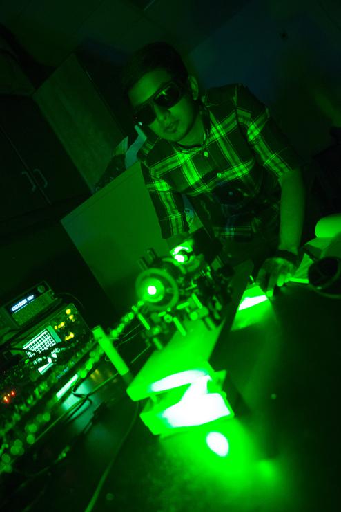 A student wearing protective eyewear uses a green laser in a physics lab.