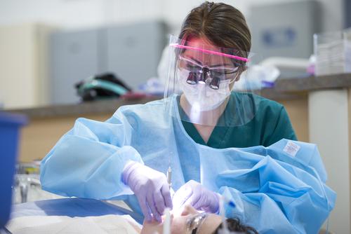 A pre-dentistry student, wearing protective equipment, works on a patient at a dental clinic.