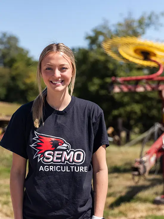 Avery, an agriculture animal science student, at the David M Barton Agriculture Research Center with crop equipment in the background