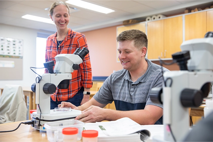 A SEMO student and faculty in the Biological and Environmental Sciences department look at a petri dish in a biology lab.