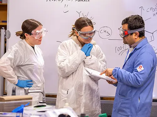 two chemistry degree students stand in front of a whiteboard going over a formula with their instructor