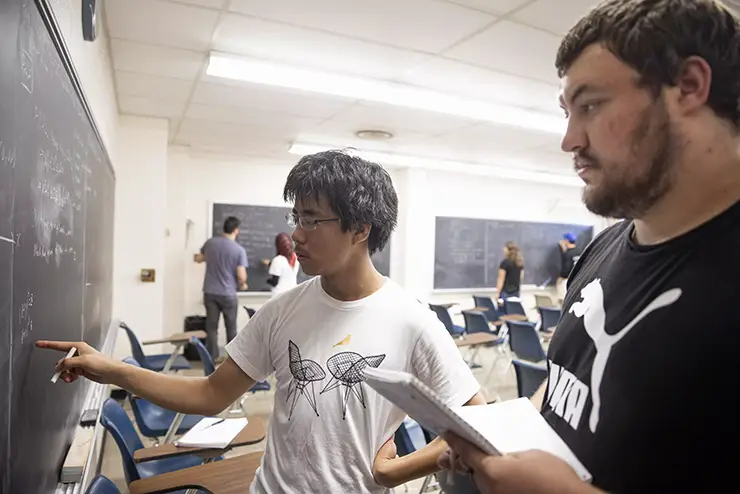 two math degree students work together at the chalkboard going through an equation