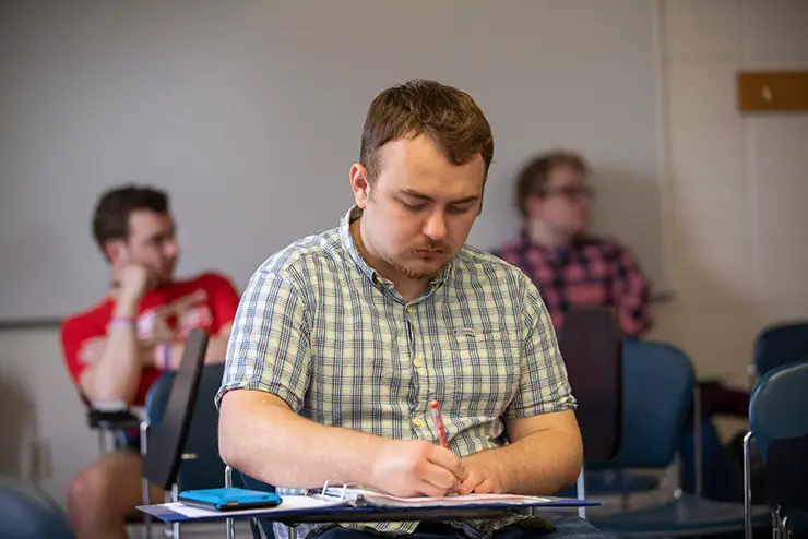 a math student sits at a desk working in his notebook