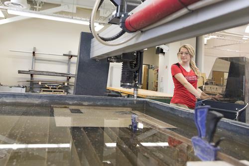 A student stands wearing safety glasses stands at a computer to being work with equipment.