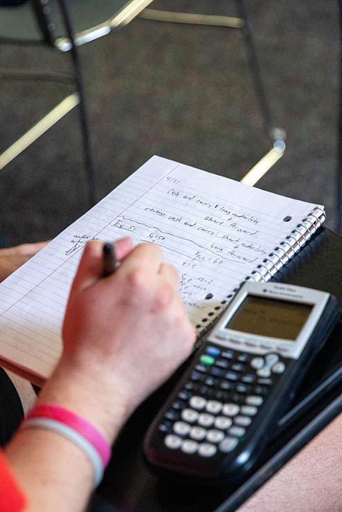 A Mathematics student sits at a desk with notebook and calculator while taking a test