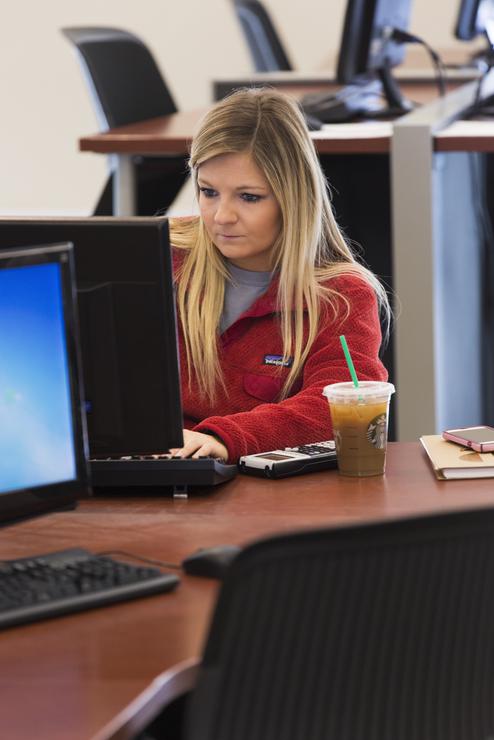A Mathematics student sits at a computer table and works on a computer.   