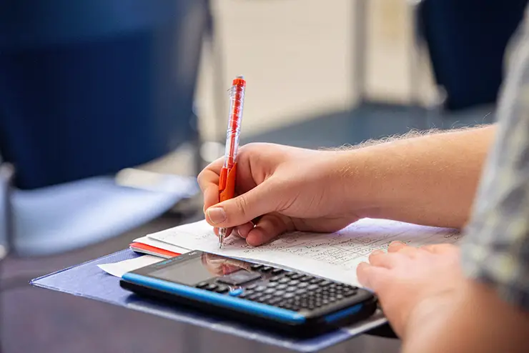 a student with notebook and calculator spread out on their desk taking notes/working problems