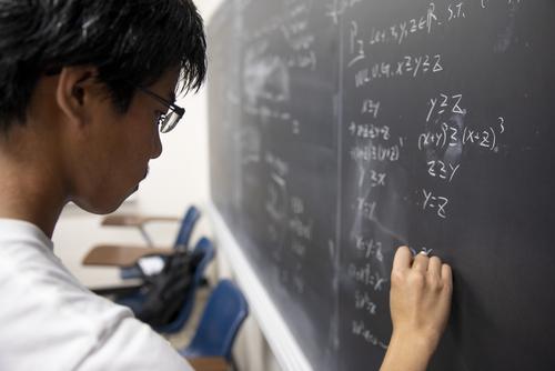 A Mathematics student writes on the chalkboard while working on an equation. 