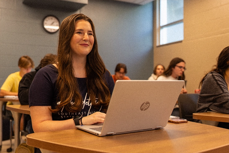 A student at SEMO sitting in a class with her laptop and smiling because this is a great program. 