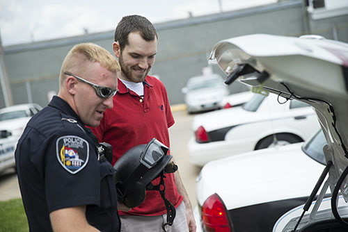 a police officer and a Police Academy student look under the hood of a car
