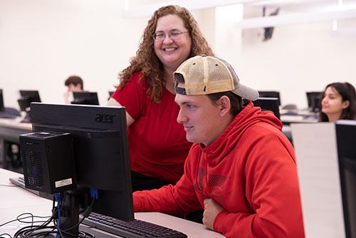 a computer science student works at a computer with a teacher looking over his shoulder