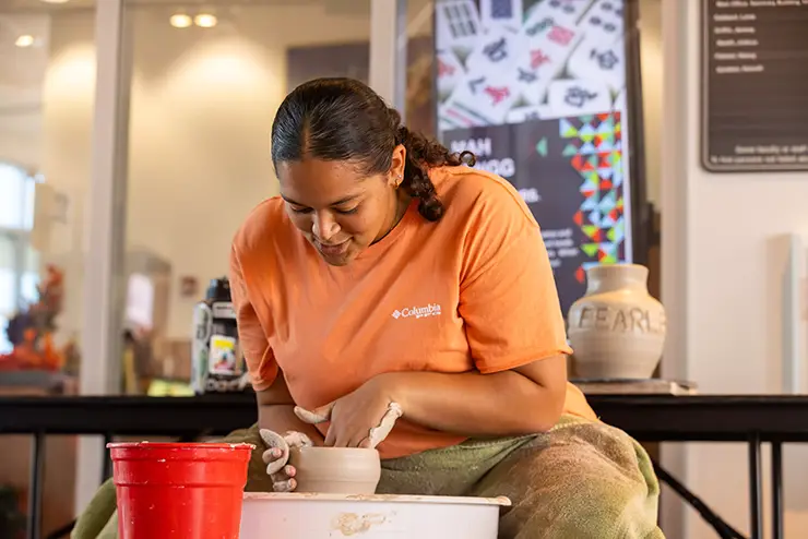 a student sits at a pottery wheel in a SEMO arts class and throws a piece of pottery