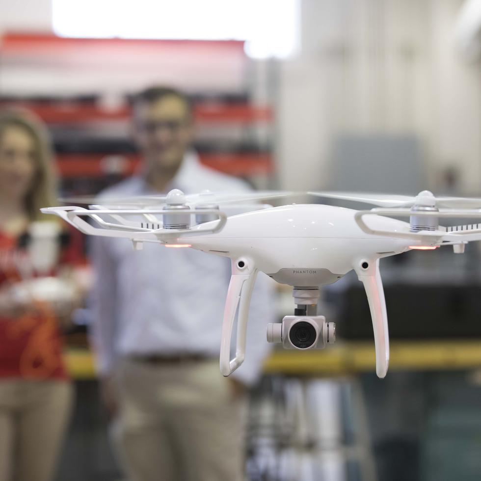 Two people stand in the background, out of focus, while in the foreground a hovering drone is in focus for the viewer. 