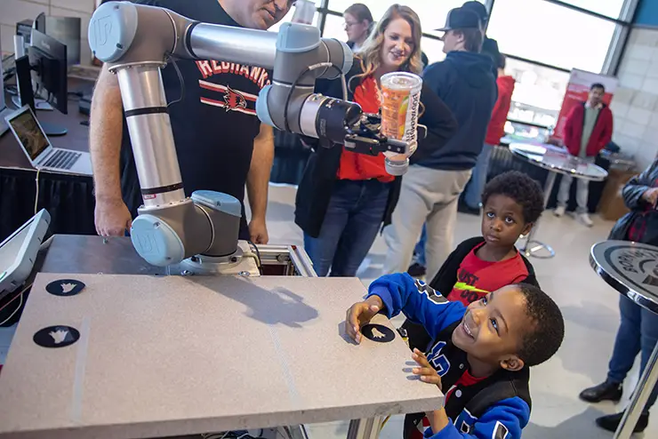two young boys grin up at a robot arm pouring out a drink
