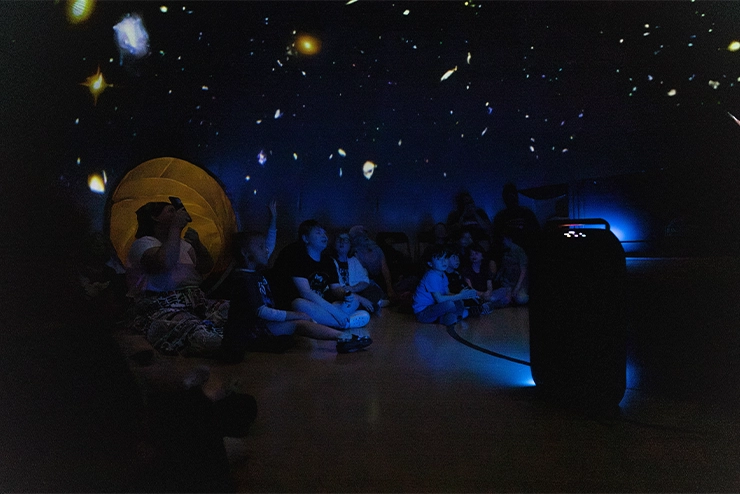 A group of children sitting in a space room which shows a clearer view projection of our solar system at SEMO