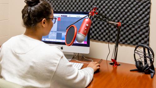 A student records voice audio inside of the Podcasting Booth within The EDvolution Center.
